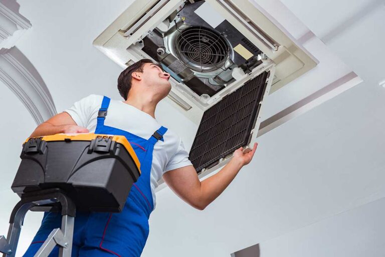 A person replacing a furnace air filter in a finished basement utility area.
