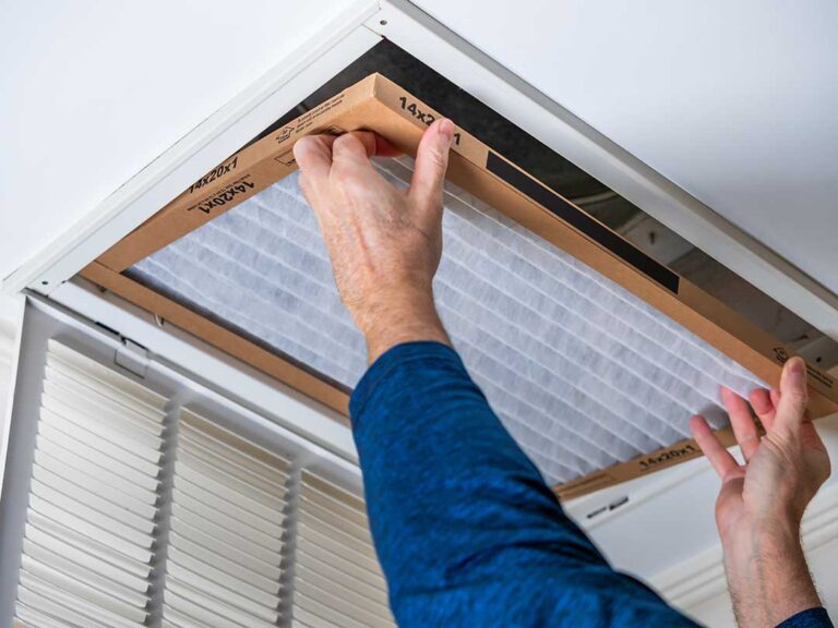 Person inspecting a vent cover and using a flashlight to look inside a home air duct.